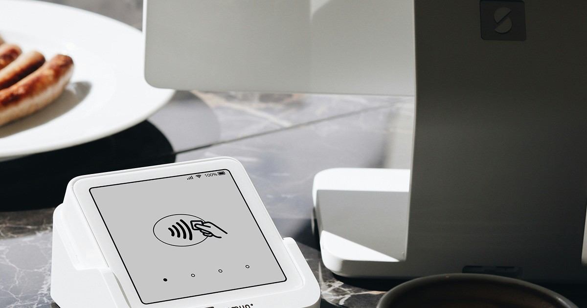 カフェのテーブルに置かれた非接触型決済端末とソーセージの乗った白い皿